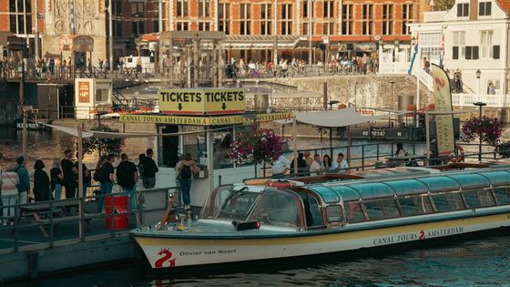 Busy canal tour dock in Amsterdam with people waiting and a boat ready for departure.