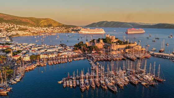 A stunning aerial photograph showcasing Bodrum's harbor, yachts, and ancient castle at sunset.
