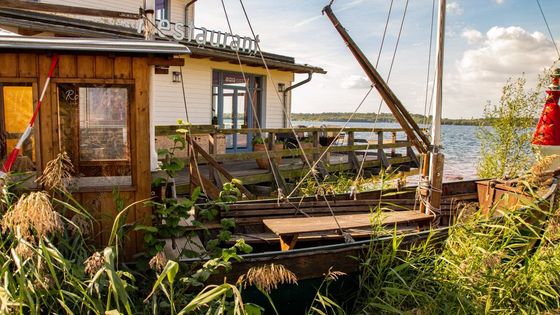 Charming rustic restaurant by the lake with a vintage wooden boat, lush greenery, and serene waters.