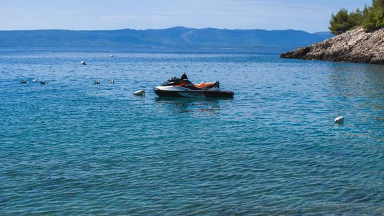 Relaxing coastal view of a jet ski on calm blue waters near a rocky coastline.