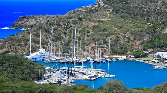 Stunning aerial view of a serene harbor with moored yachts, surrounded by lush hills and vibrant blue water.